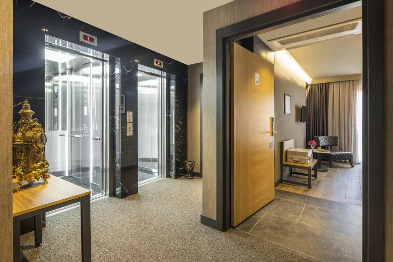 Il pianerottolo dell'ascensore all'Hotel Marius, con un orologio dorato lavorato e la porta di una camera aperta